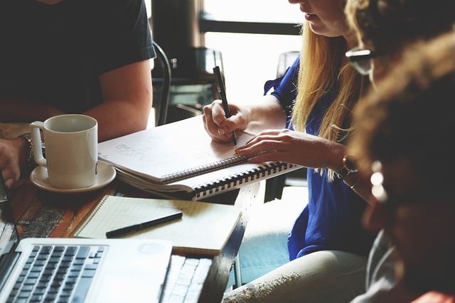 Photo of a meeting with a laptop, pad and paper and a coffee mug.